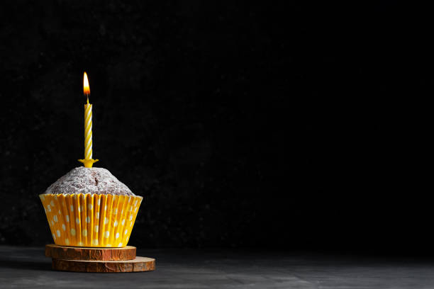istock One cupcake in a paper cup with a yellow candle with flame on a dark background copy space birthday card 1297532863