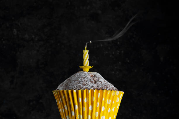 istock Birthday cupcak in paper cup with extinguished candles on a dark background 1297532864