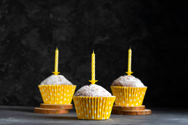 istock Three birthday cupcakes in paper cups with extinguished birthday candles on dark background 1297532873