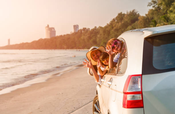 Happy family young woman with her daughter and son sitting in white car with hand up and look out from windows Happy family young woman with her daughter and son sitting in white car with hand up and look out from windows on the beach. Family holiday travel concept. road trip stock pictures, royalty-free photos & images