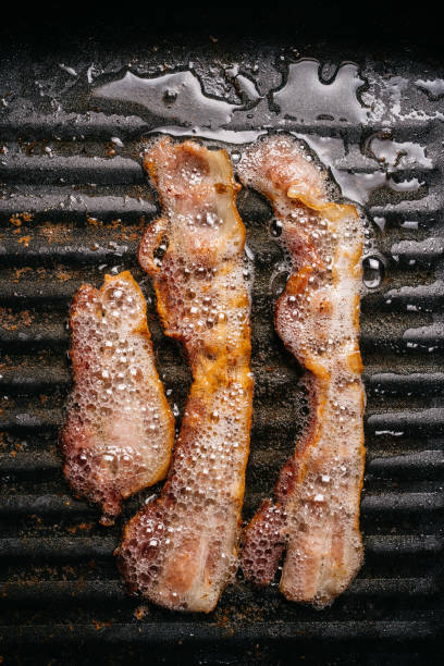 vista superior de las tiras de tocino chisporroteantes en una sartén con aceite de tocino caliente para hacer tocino crujiente. comida de keto. - grasa saturada fotografías e imágenes de stock