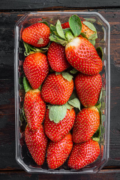 istock Transparent plastic tray with freshly picked strawberries, on old dark  wooden table background, top view flat lay 1297534149