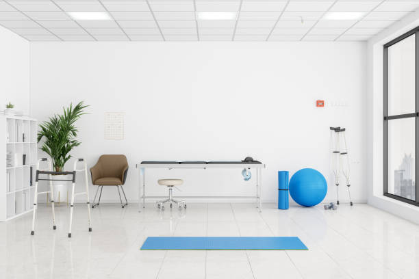 interior de uma sala de fisioterapia com mesa de exame, andador de mobilidade, muleta, bola de ginástica de cor azul e tapete de exercício. - doctors office examination room examination table office - fotografias e filmes do acervo