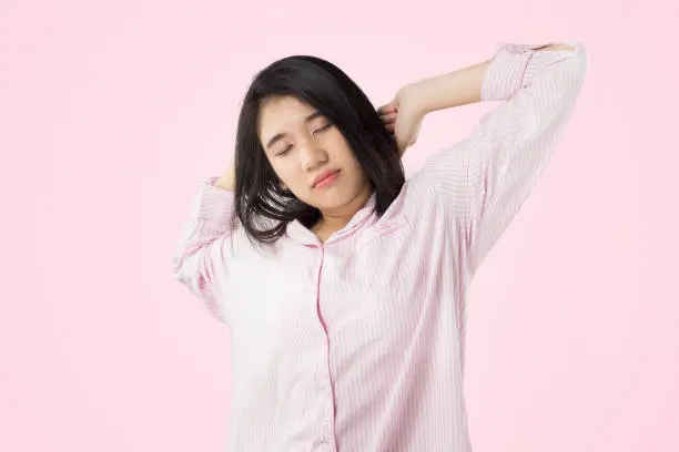 young asian woman wear pink pajamas yawn and stretch when her wake up feeling sleepy