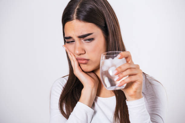 mujer joven con dientes sensibles y vaso de agua fría con hielo. concepto de salud. mujer bebiendo bebida fría, vaso lleno de cubitos de hielo y siente dolor de muelas, dolor - dientes humanos fotografías e imágenes de stock