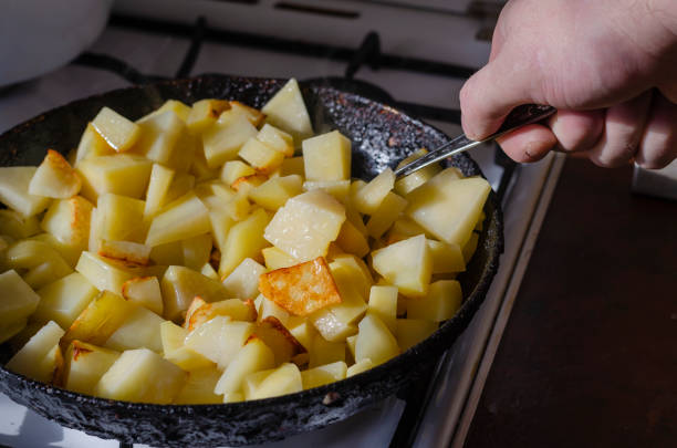 istock Man's Hand with a spoon stirs sliced potatoes in a pan on the kitchen stove. 1297549030