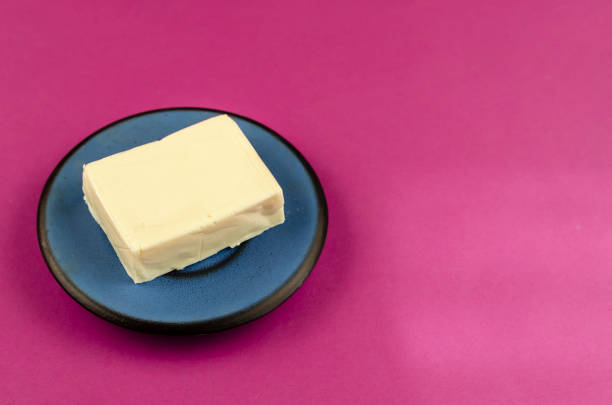 istock Rectangular piece of processed cheese in a blue saucer on a pink background. 1297549096