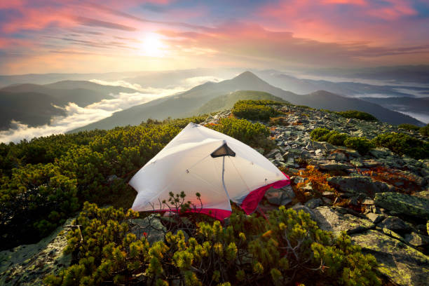 Morning dawn after rain with fog on the alpine stone wastelands of the Gorgan of the Carpathians of Eastern Europe. White tent glows in the rays of dawn over a misty valley