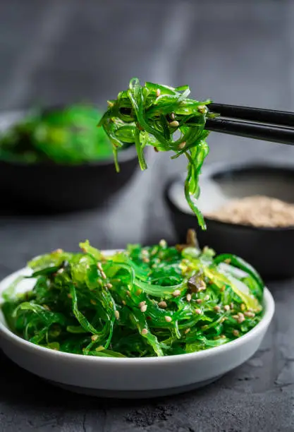 Traditional Japanese wakame salad with sesame seeds on black background. Healthy and fresh seaweed salad.