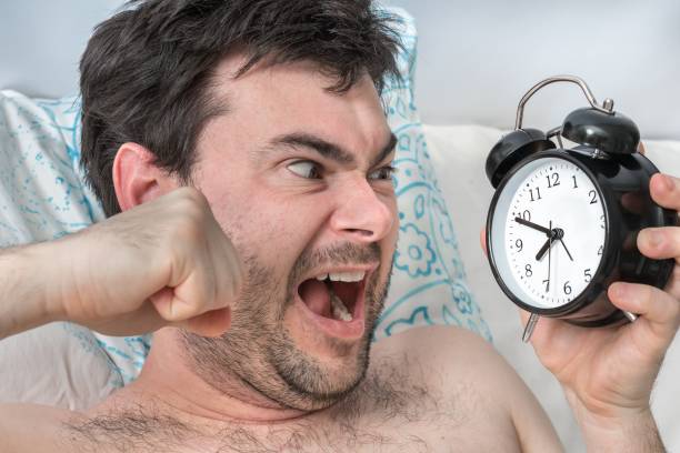 istock Angry man with alarm clock does not want waking up 1297558329
