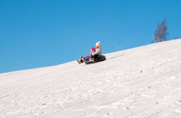 family on vacation in winter. a woman and a child, 5 years old, caucasians, quickly ride down a snow-covered slide on an inflatable ring. - 35 40 years fotos imagens e fotografias de stock