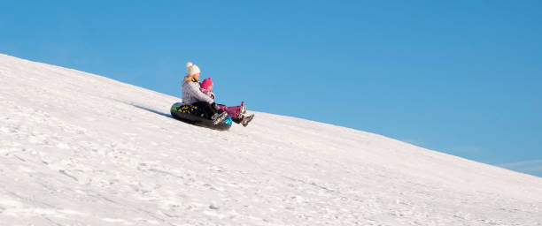 eine frau und ein kind, 5 jahre alt, kaukasier, fahren schnell eine schneebedeckte rutsche auf einem aufblasbaren ring hinunter. - child winter snow 4 5 years stock-fotos und bilder