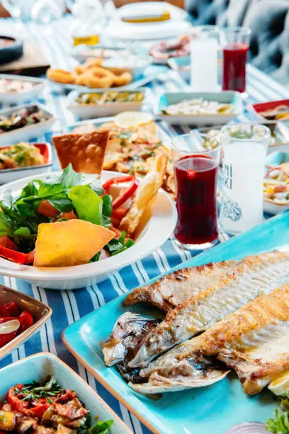 Seafoods, grilled meat, meze, herbs, fish, raki, ouzo, appetizers and salads in Greek or Turkish Fish Restaurant on the table for dinner or lunch at the beach from Greece or Turkey.