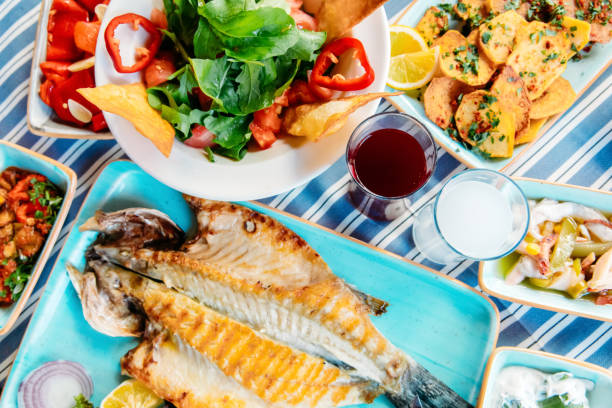Grilled fish, salads and vegetables. Seafoods, grilled meat, meze, raki, ouzo, appetizers and salads on the table in Greek or Turkish Fish Restaurant for dinner or lunch at the beach.