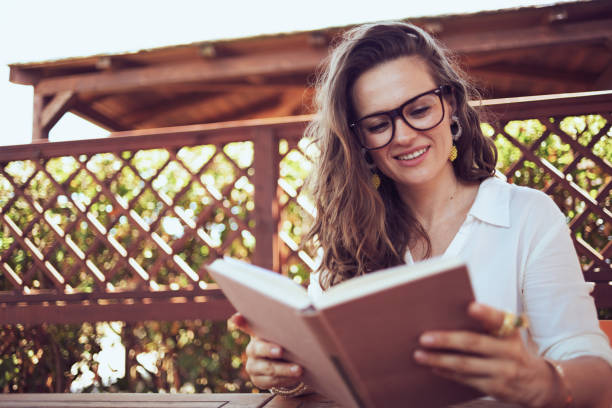 istock smiling woman in shirt sitting at table reading book 1297561840