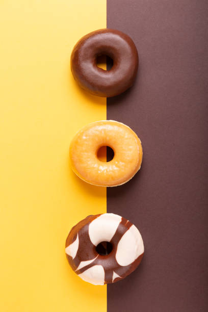 istock Flat lay composition of three donuts on brown and yellow background. vertical format. 1297565865