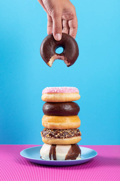 istock Hand holding bitten donut and stack of diferent donuts on pink and blue background. 1297565883