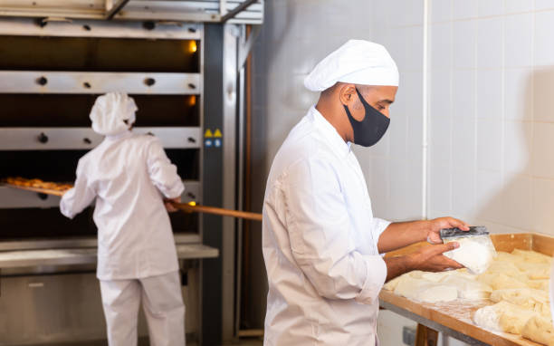 istock Bakery worker in protective mask cuts raw dough with knife to prepare for baking 1297569753