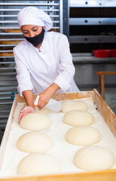 istock Female baker sprinkling shaped bread loaves with water before baking 1297569755