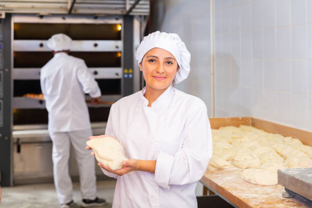 istock Smiling female baker holding raw dough in bakery workshop 1297569759
