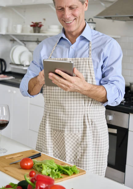 istock Happy old senior man using tablet preparing vegetable salad in kitchen, doing online shopping, searching cook book diet recipes, ordering food online, watching videos preparing healthy food at home. 1297569947