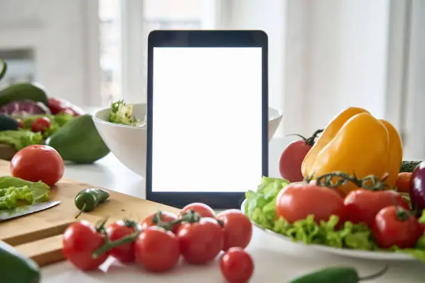 Photo of Digital tablet computer with mockup white screen on vegetarian healthy food vegetable background. Online grocery shopping delivery app ads concept, cook book diet plan nutrition recipes, close up view