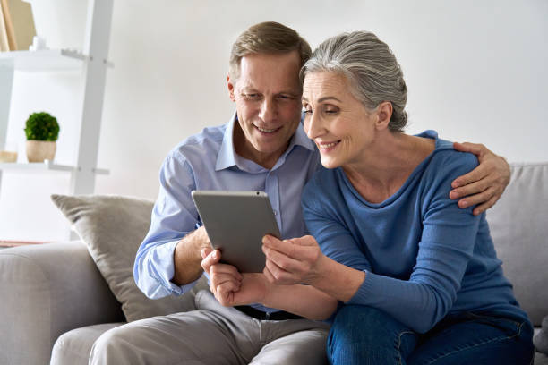 istock Happy old senior retired grandparents using digital tablet sitting on couch at home. Smiling mature 50s family couple enjoying websurfing online holding computer technology device making video call. 1297569985