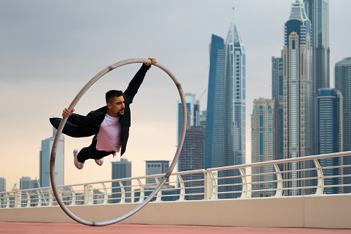 Cyr Wheel artist wearing black and white smart clothes with cityscape background of Dubai during sunset.