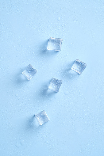 Shiny ice cubes and water drops on blue background. Top view.