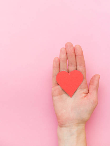 istock A woman's hand holds a red paper heart on a pink one, top view 1297573239