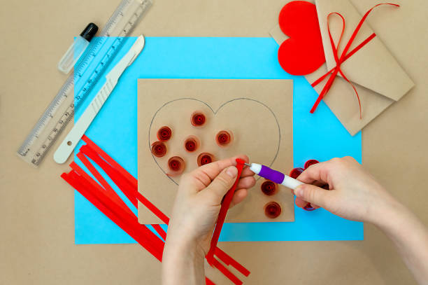 발렌타인 데이를 위한 공예품. 퀼링 방법을 사용하여 심장을 만드는 것입니다. 하트가 있는 카드를 만들기 위한 단계별 지침입니다. 5 단계 - 아이의 손으로 awl을 사용하여 종이 나선형형성. - pencil colors heart shape paper 뉴스 사진 이미지