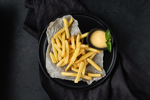 French fries with cheese sauce on black background, top view