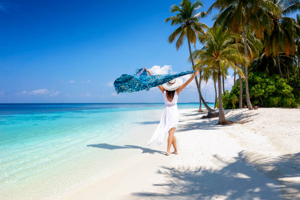 una mujer con vestido blanco de verano camina en una playa tropical paradisíaca - wind scarf women people fotografías e imágenes de stock