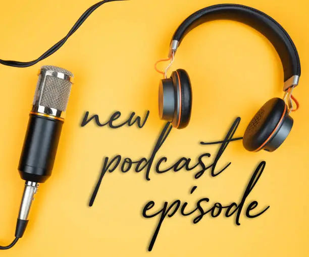 directly above view of microphone and headphones on orange background with text NEW PODCAST EPISODE, podcast recording concept