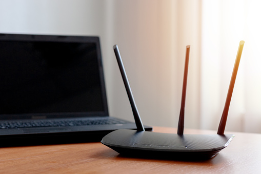 wireless wifi router near laptop on wooden table indoors. window behind. backlit. wireless connection concept. internet service conceptual.