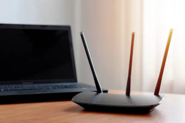 wireless wifi router near laptop on wooden table indoors. window behind. backlit. wireless connection concept. internet service conceptual.