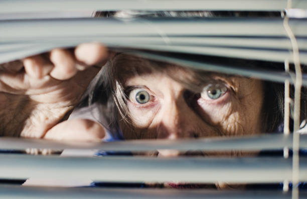 istock Senior woman peering anxiously through blinds 1297577598