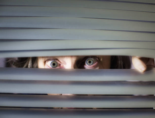 istock Senior woman peering anxiously through blinds 1297578049
