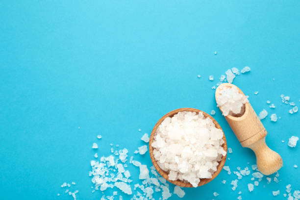 istock Sea salt in bowl and spoon on blue background 1297578234