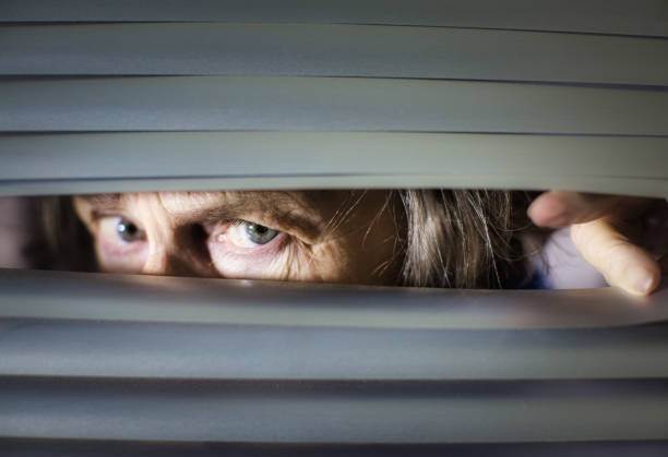istock Senior woman peering anxiously through blinds 1297578619