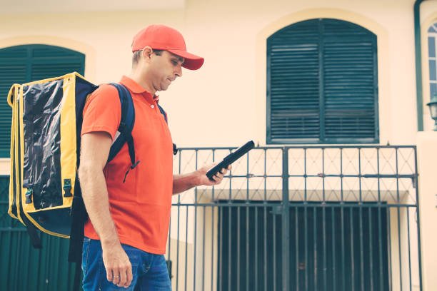 istock Serious courier watching address on tablet, holding clipboard 1297579419