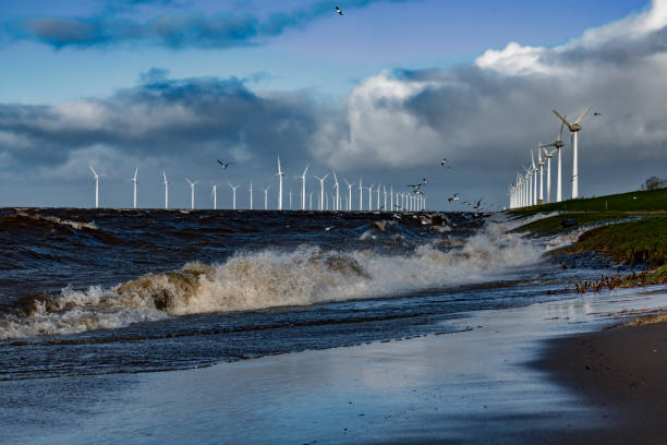 istock Wind turbines on land and offshore in a storm with waves hitting the shore 1297581313