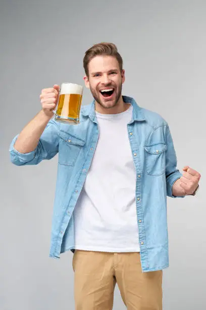 Photo of Young Man holding wearing jeans shirt holding glass of beer standing over Grey Background