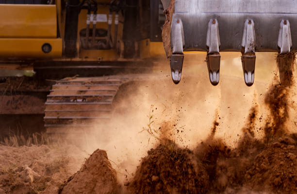 Selective focus on metal bucket teeth of backhoe digging soil. Backhoe working by digging soil at construction site. Crawler excavator digging on soil. Earth moving machine. Excavation vehicle.