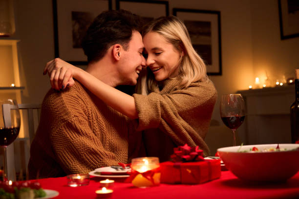 istock Happy smiling affectionate young couple in love hugging laughing, drinking wine, talking, celebrating Valentines day dining together, having romantic dinner date in candle light sitting at home table. 1297583758