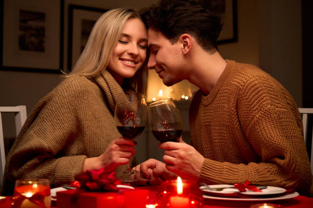 istock Happy young couple in love clinking glasses drinking red wine having romantic dinner date celebrating Valentines day evening or enjoying anniversary sitting at table at home or in restaurant. 1297583776