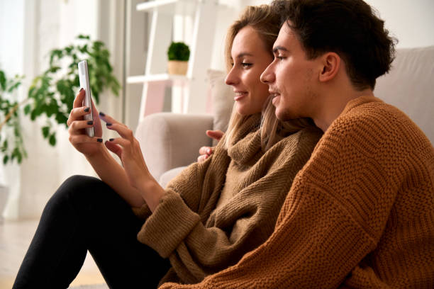 istock Young happy couple customers holding smartphone using mobile cell phone at home, doing online shopping in ecommerce app together, ordering food delivery, checking social media applications together. 1297583793
