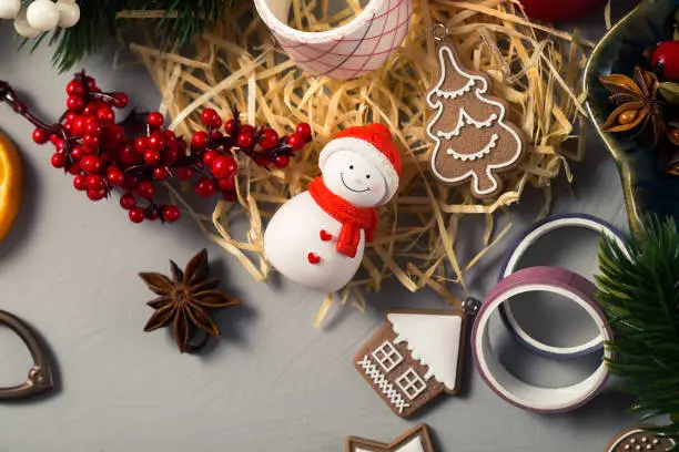 Photo of Christmas items on the table with a view from above. Snowman figurine, fir twigs, decorations in the form of ginger cookies, holly berries and more
