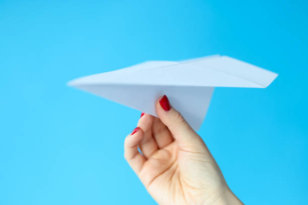 istock Female hand holding paper plane on blue background 1297589830