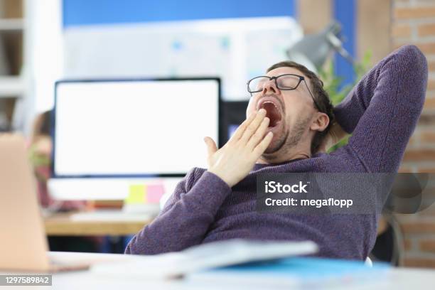 Young Man Siting At Table In Office And Yawning Stock Photo - Download Image Now - Yawning, Laziness, Wasting Time